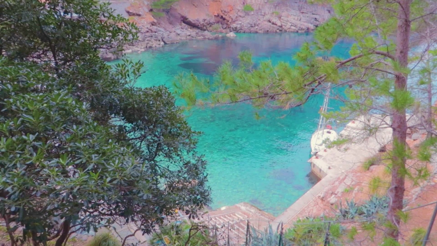 A top view of an island over the trees with crystal clear green water, surrounded with mountains.