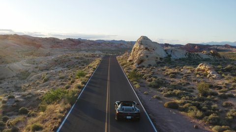 Nevada / United States - 05 24 2019: Black Ferrari driving along a twisting road in the Valley of Fire at sunset. Aerial tracking shot