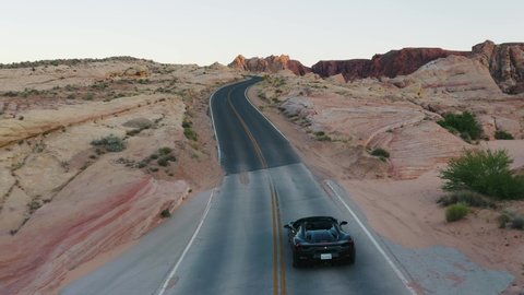 Nevada / United States - 05 24 2019: Black Ferrari 488 driving up a hill through the Valley of Fire, Nevada, at sunset. Aerial tracking shot