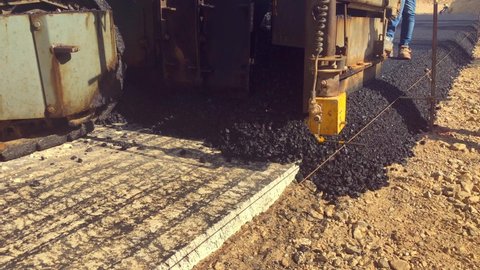 Asphalt paver machine lays asphalt mix on concrete base during road construction