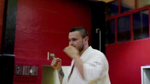 KAZAN, TATARSTAN/RUSSIA - JUNE 30 2020: Bearded karate trainer with tattoo in white traditional kimono explains strike to students in light contemporary gym on June 30 in Kazan