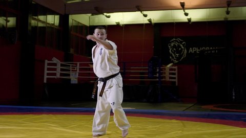 KAZAN, TATARSTAN/RUSSIA - JUNE 30 2020: Karate master in white traditional kimono does leg kicks with jumps on tatami at training in contemporary gym on June 30 in Kazan