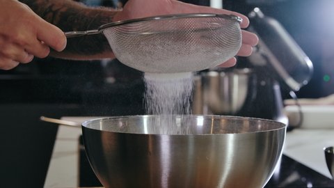 Close-up Cook is Sifting Flour through Sieve for Baking Mixing Ingredients in Metal Bowl. Conception Cooking Baking and Confectionery. Preparing Flour to Baking Bread in Kitchen at Home Slow mo 4k