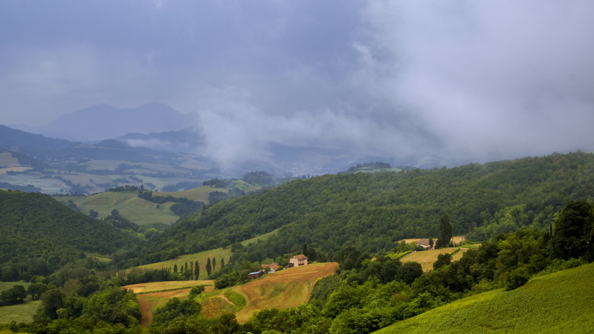 Wind blowing rain storm clouds timelapse over fields and hills in Italy, summer nature outdoor landscape panorama view. Green and yellow grass, natural scenery. High quality 4k footage