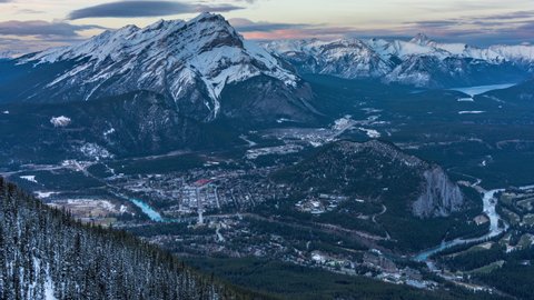 Town of Banff sunset time view in snowy winter season. Colorful clouds, Cascade Mountain and surrounding mountains in background in dusk. Banff National Park, Alberta, Canada. 4K Time-lapse zoom in.