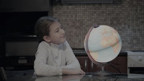 Child looks at the globe and dreams of traveling. The schoolgirl spins an imaginary holographic globe from which palm trees and magic planes appear