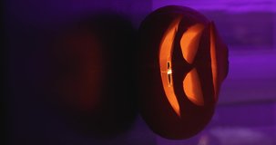 Vertical video of pumpkin glowing inside jack lantern face at neon pink blogger background. Traditional orange carved pumpkin symbol with bright lights on night party. Jack-o-lantern at home party.