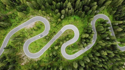 Aerial top down drone shot above the winding mountain road between the trees near Passo Giau in Dolomites, Italy. Overcast late summer weather. Car driving through the curve 4K. Flying straight up