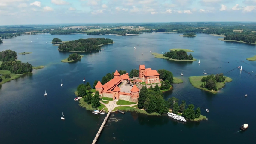 Aerial drone shot of red brick medieval castle on island in Trakai, Vilnius region, Lithuania. Sunny midday summer weather with some boats on the lake. Point of interest orbit camera movement POI 4K | Shutterstock HD Video #1062111634