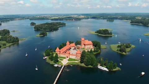 Aerial drone shot of red brick medieval castle on island in Trakai, Vilnius region, Lithuania. Sunny midday summer weather with some boats on the lake. Point of interest orbit camera movement POI 4K