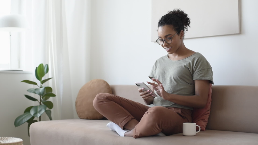 Woman using smartphone at home. African american student girl texting on mobile phone in her room. Communication, work or study from home, connection, mobile apps, technology, lifestyle concept | Shutterstock HD Video #1062111727