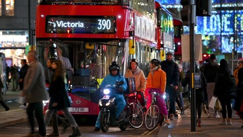 LONDON - NOVEMBER 3, 2020: Cyclists, a motor scooter and red London Double Decker buses pulling away from traffic lights beneath the Oxford Street Christmas lights at night