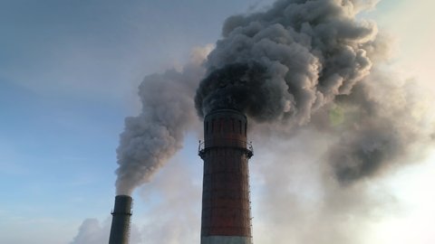 Very dirty dark smoke comes out in horrific clouds from old chimney of factory plant, polluting environment. Toxic production company. Industrial enterprise. Winter. Aerial gain attitude close up