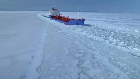 Drone sideways close steel grand icebreaker cinematic iceboat floats breaks snowy ice in frozen endless sea, made an expedition to Arctic North. Contrast red blue deck. Horizon open space. Travel 