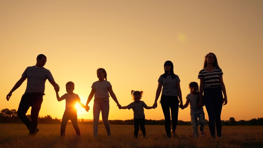 Happy big family in Park at sunset. People on walk have fun. Mom dad son and daughters walk together in field. People holding hands, teamwork. Family trip on foot. Happy big family concept