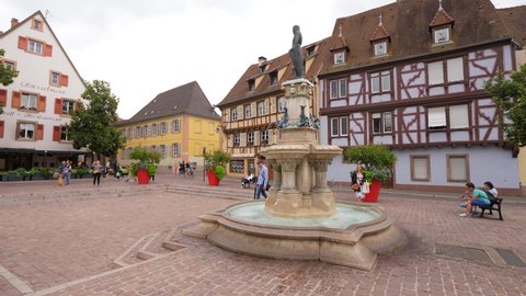 COLMAR, FRANCE - AUGUST 17, 2019: The Roesselmann Fountain at Six-Montagnes-Noires square, Colmar landmark, camera move around. Characteristic half-timbered houses seen on background