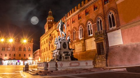 Time lapse of Neptune statue in Bologna at the night moment. It is see the fountain in close up and the red build in the main square in background with i full moon in the sky 