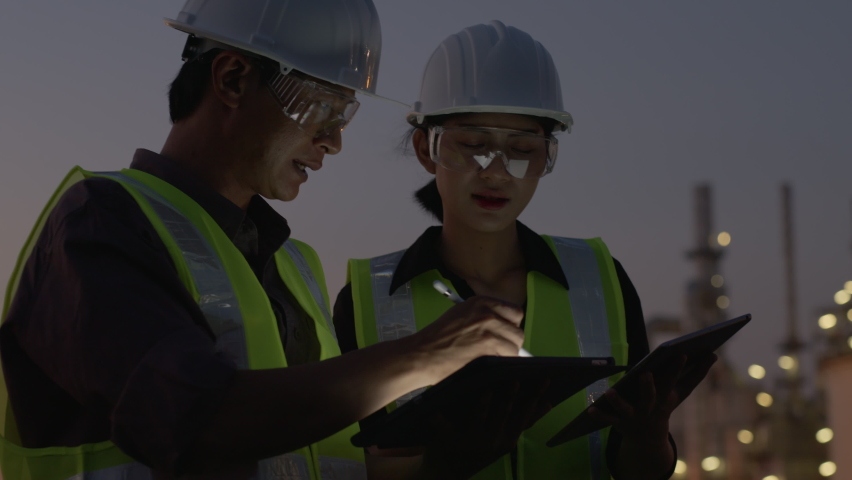 Medium shot. two Asian engineers using digital tablet working and going through routine checks, late a night shift at petroleum oil refinery in industrial estate Royalty-Free Stock Footage #1062126037