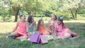 Happy group of kids celebrating a birthday in the garden with a whistle. Girls in beautiful dresses. 4k video.