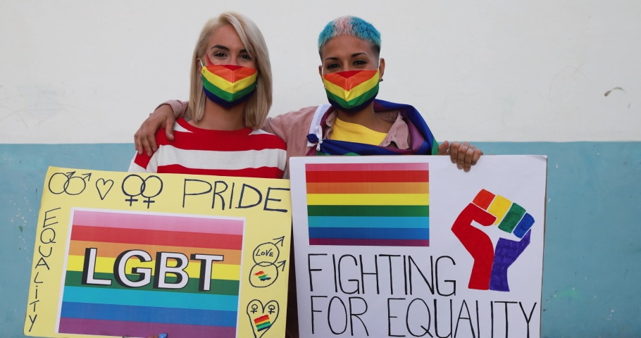 Women gay couple holding lgbt banners while wearing mask at pride protest