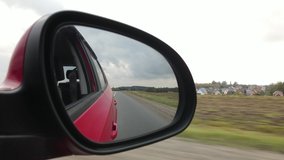 Red automobile in motion, the road is reflected in the long-distance mirror of the car