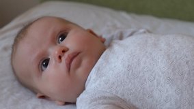 Close up video of an infant newborn girl lying in bed wearing pajama looking somewhere