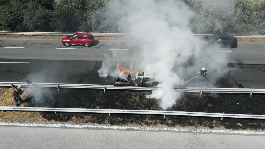 Firefighters extinguish burning car on highway following serious car accident on hot summer day aerial view. Fire truck came to rescue. Flow of cars on track. Problem is on road. Traffic incident