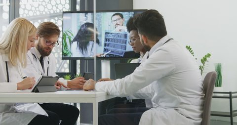 Good-looking confident multiracial successful male and female doctors working together in boardroom during online conference with their medical partners