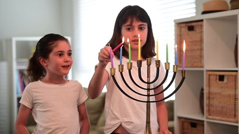 Two happy Jewish sisters lit a menorah candelabra on the eight day of Hanukkah Jewish holiday. 