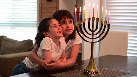 Two happy Jewish sisters looking at a beautiful menorah candelabra glowing on the eight day of Hanukkah Jewish holiday. 
