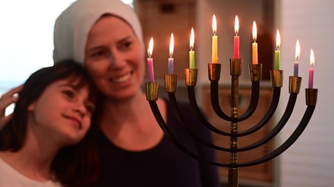Happy Jewish mother and daughter looking at a beautiful menorah candelabra glowing on the eight day of Hanukkah Jewish holiday. 