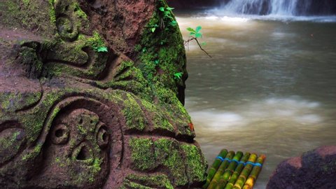 Beautiful waterfall hidden in tropical rainforest jungle with bamboo raft on background scenery stone carving stone in Maya style. 4K Travel in wild nature