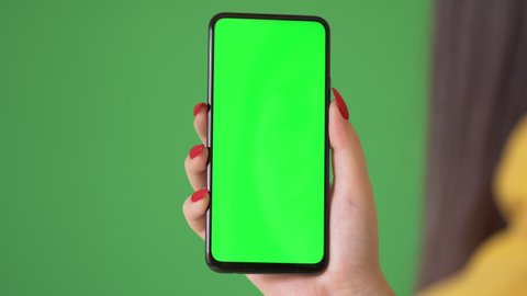 Woman hand holding the smartphone on green screen chroma key background. Mobile phone mock-up for your product. The iPhone Xr model in vertical orientation portrait mode