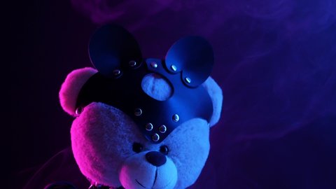 toy bear dressed in leather belt harness accessory for BDSM games on a dark background in neon light in the smoke