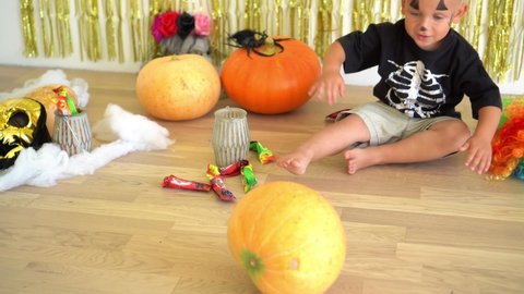 Cute little boy in skeleton costume playing with pumpkin at home. Preparing for Halloween celebration. Mask pumpkin and other decorations. Camera movement shot with gimbal.