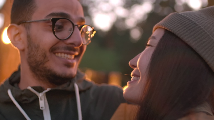 Close up of romantic multi-ethnic couple talking and smiling while looking at each other at beautiful location decorated with lights on summer evening