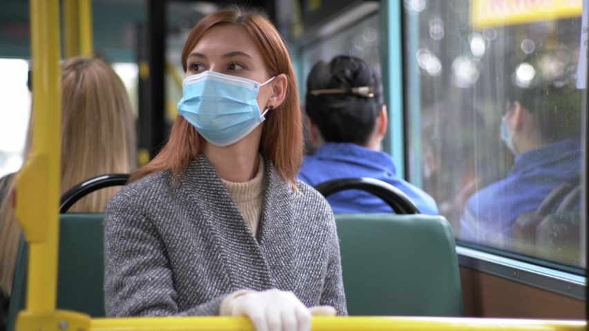 Precautions, young woman wearing gloves observes safety precautions and puts on medical mask to protect against virus and infection while traveling in city bus, pandemic | Shutterstock HD Video #1062160885
