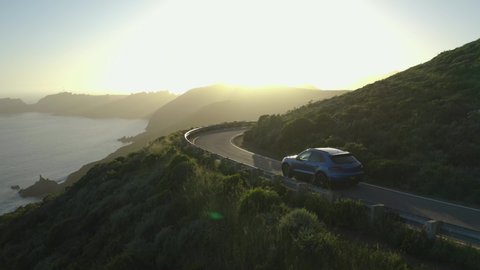 San Fransisco / United States - 04 24 2019: Blue Porsche Macan driving along an ocean road in San Fransisco at sunset
