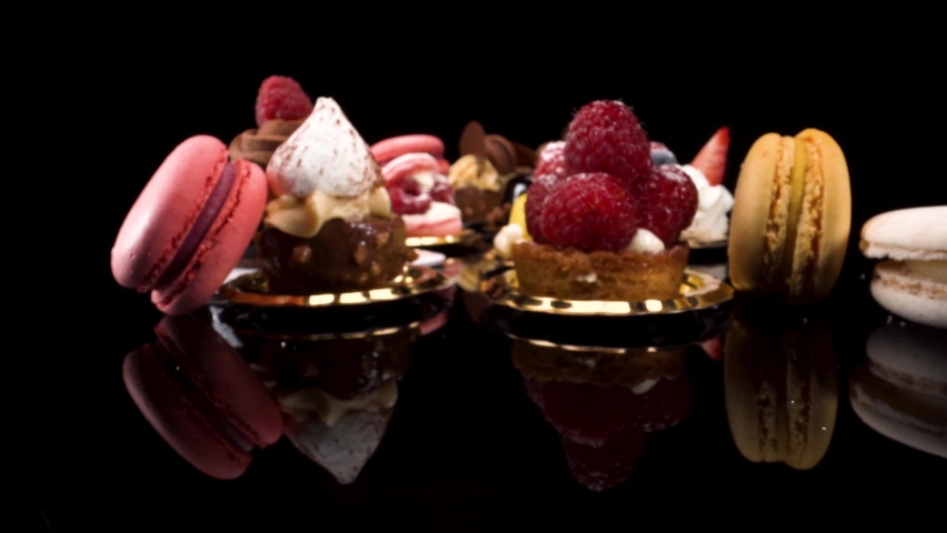 Macro view moving past patisserie on black reflective background, probe lens view of sweet pastry and small cakes | Shutterstock HD Video #1062162052