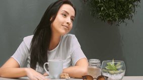 Wide 4k video of a young, beautiful, Latin Hispanic woman drinking coffee in garden cafe or home patio. 