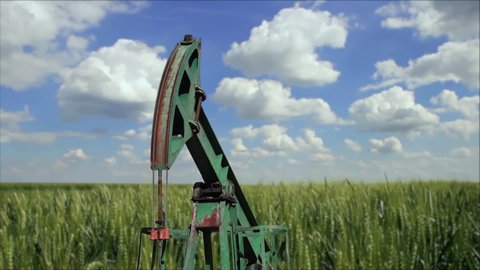 Oilfield Pump Jack in a Crop Field of Wheat. Extraction of Petroleum. Fossil Fuel Energy. Oil Industry Equipment. Crude Oil Pumping Unit.