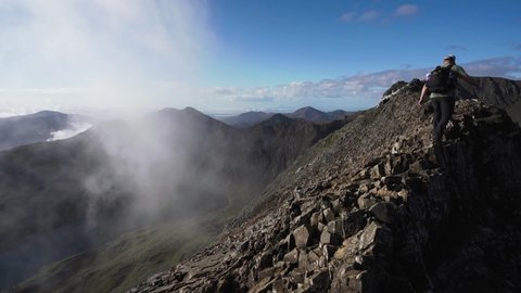 Man climbing Crib Goch mountain ridge towards mount Snowdon in North Wales with low cloud