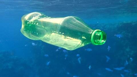 Plastic pollution, plastic bottle in blue water. Discarded green plastic bottle slowly drifting under surface of blue water near coral reef. Plastic garbage environmental pollution problem in Red Sea