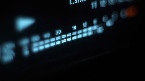 Glowing blue stereo level recording music, speech, other sound on the front panel of audio equipment, on a black background. Closeup