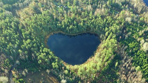 Heart shaped lake in forest. Tilting drone shot of natural wonder in nature environment. Symbol sign for love peace save the our planet in Swedish woods. blue pond water with special shape in Sweden. 