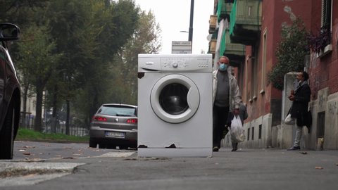 Italy , Milan November 2020 - washing machine abandoned on the street in the Giambellino district, illegal landfill and degradation in the urban suburbs - people walk among the waste on the sidewalk 