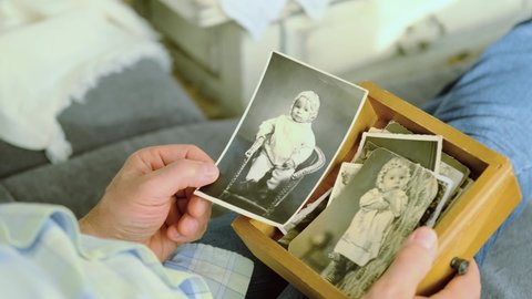 an elderly man looks through his old photographs of 1960-1970, the concept of nostalgia and memories of youth, childhood, remembering his life, relatives, family connection of generations