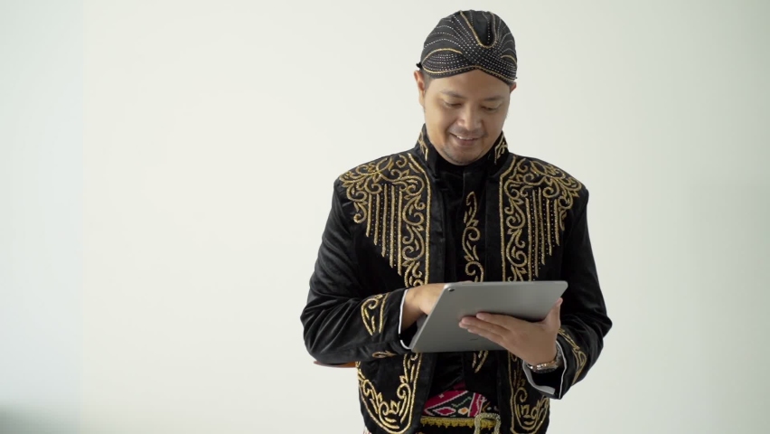 happy traditional Javanese man holding a tablet wearing beskap