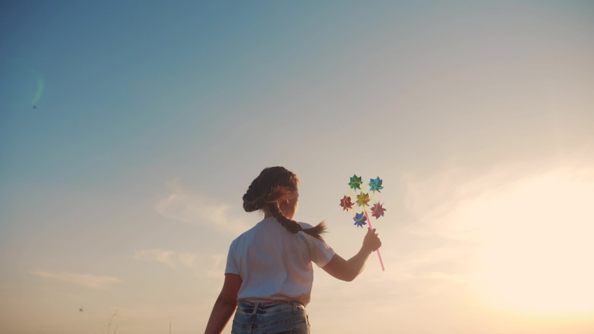 dream concept. little girl kid run near the field at sunset silhouette with holds in hands toy turntable pinwheel. lifestyle happy family kids concept. happy daughter runs along rural road to meet the Royalty-Free Stock Footage #1062177661