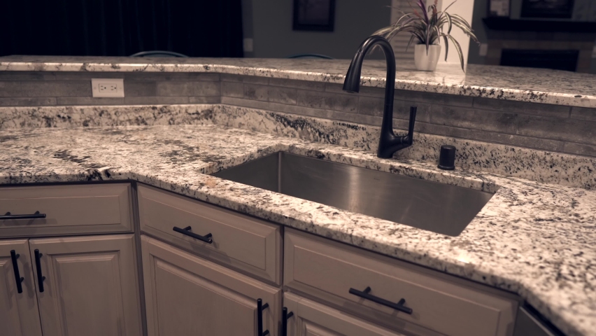 Contemporary kitchen cabinet design with counter top made of granite stone, under mount sink and faucet. Kitchen countertops are in white and gray colors. Royalty-Free Stock Footage #1062182362